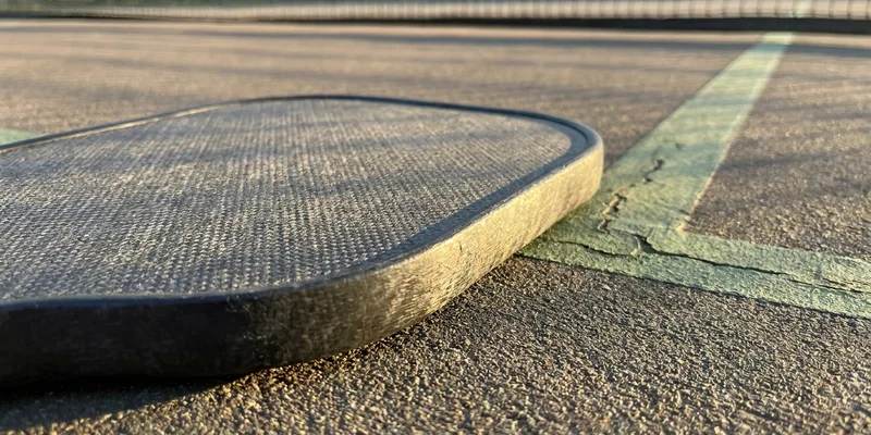 thick-core pickleball paddle close-up with dramatic side light on a court